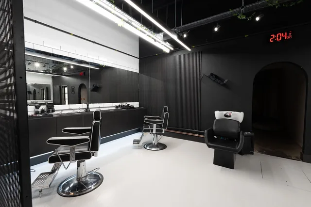 A barber chair and a backwash basin against the black panelled wall at the rear of the shop.